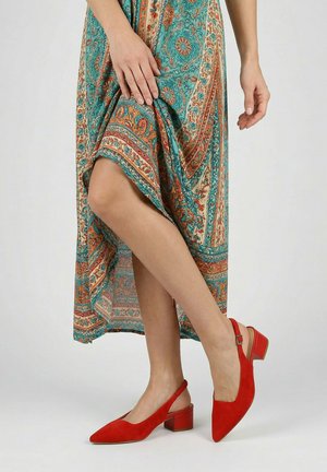 Frau trägt einen gemusterten Rock in Türkis und Orange, leicht angehoben, um rote Slingback-Pumps mit Blockabsatz zu zeigen.