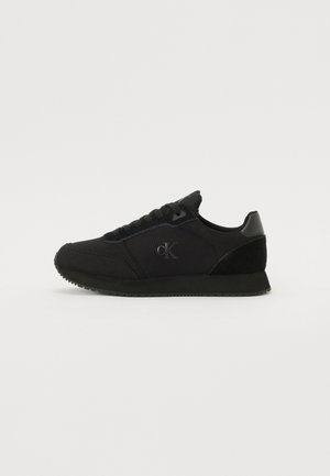 Black athletic shoes with a combination of fabric and suede materials, featuring a lace-up design and a logo detail on the side.