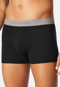 Zwarte boxershorts met een grijze elastische tailleband waarop het logo "SCHIESSER" staat. Soepele katoenen stof en een aansluitend ontwerp.
