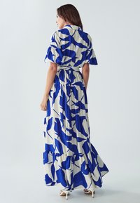 Maximekkonen, jossa on sinivalkoinen abstrakti kuvio, leveät hihat, kerroksellinen helma ja vyötäröllä vyö, kevyessä kankaassa.