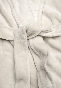 Mjuk, plysch beige badrock med knytbälte. Har en slät yta och vikta tygkanter. Inga tydliga mönster eller detaljer synliga.