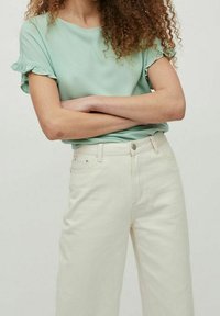 Haut vert menthe à manches courtes avec détails à volants, associé à un jean large taille haute couleur blanc cassé. Coupe décontractée et confortable.