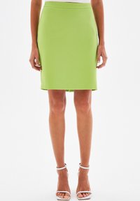 Pistáciově zelená přiléhavá sukně s hladkou texturou, délka ke kolenům, s jednoduchým pasem bez viditelných vzorů nebo ozdob.