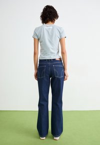 Hele sinine lühikeste varrukatega slim-fit t-särk, millel on logodetail seljal, kombineeritud tumedate siniste laienevate teksadega, millel on tagataskud ja õmblused.