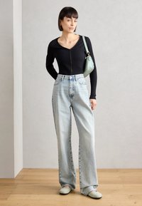 Top negro de manga larga acanalado con cremallera, jeans de pierna ancha de lavado claro y bolso verde menta, combinados con zapatos de lona verde claro.