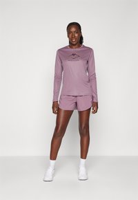Atletická souprava s dlouhým rukávem v purpurové barvě, na které je horské logo, a odpovídající purpurové šortky, vyrobené z lehkého materiálu.