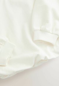 Felpa color crema con polsini a costine, realizzata in un tessuto morbido e dalla forma rilassata. Dettagli di texture limitati visibili nel tessuto.