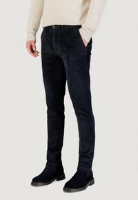 Pantaloni in velluto a coste color blu scuro con vestibilità slim, dotati di chiusura con bottoni e tasche anteriori. Indossati con stivaletti neri alla caviglia e un maglione leggero.