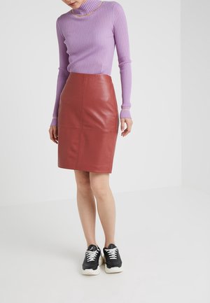 Pull à col roulé côtelé violet associé à une jupe crayon en cuir rouge ajustée. Le mannequin porte des baskets noires, affichant un look décontracté.