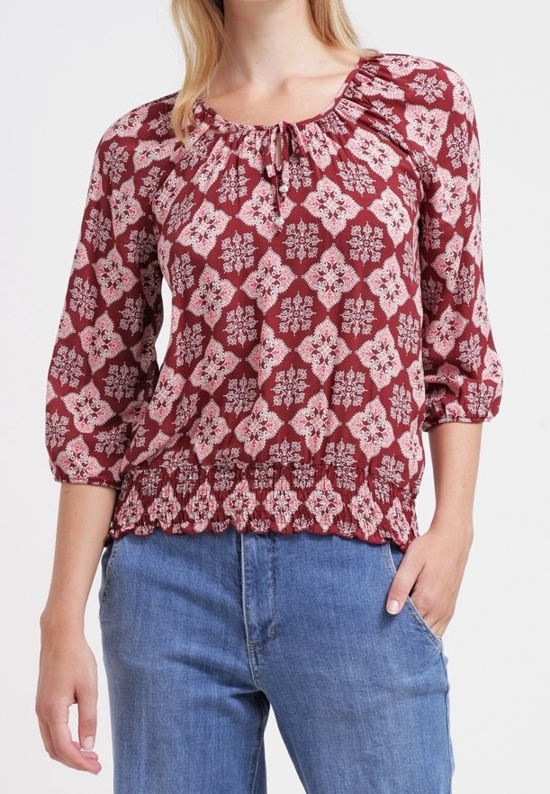 Blouse bordeaux avec motif floral blanc, décolleté en scoop avec détail froncé, et manches 3/4 ; présente un ourlet peplum et un tissu texturé.
