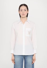Witte blouse met lange mouwen van lichtgewicht materiaal, met een borstzak voorzien van een ingewikkeld beige monogramontwerp, een klassieke kraag en knoopsluiting.