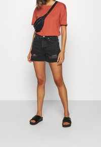 Tyrkysové tričko, černé denimové kraťasy s roztržením a černá krosbody taška. Černé skluzné sandály dokončuj�í outfit.