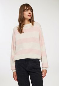 Sweter dzianinowy z poziomymi paskami w jasnym różu i kremowym. Lekko oversize, z wysokim kołnierzem oraz ściągaczami przy mankietach i u dołu.