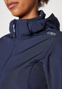 Veste softshell bleu marine avec col montant, fermeture éclair frontale et logo CMP. Caractérisée par une texture lisse et des lignes élégantes, adaptée à une utilisation en extérieur.