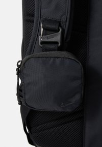 Black nylon backpack featuring adjustable straps, a textured mesh panel, and a small zippered pocket with Nike branding. Side detail visible.