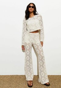 Gehaakt twee-delen set in ivoorkleur, bestaande uit een cropped langemouwen top en flared broek met diamantpatronen, gestyled met zwarte zonnebril.