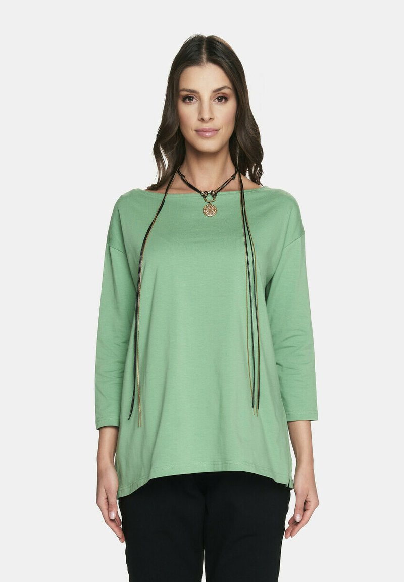 Jasnozielona bluzka z długim rękawem o dekolcie w kształcie łodzi i luźnym kroju. Posiada wisiorek na czarnych sznurkach jako dodatkowy detal.