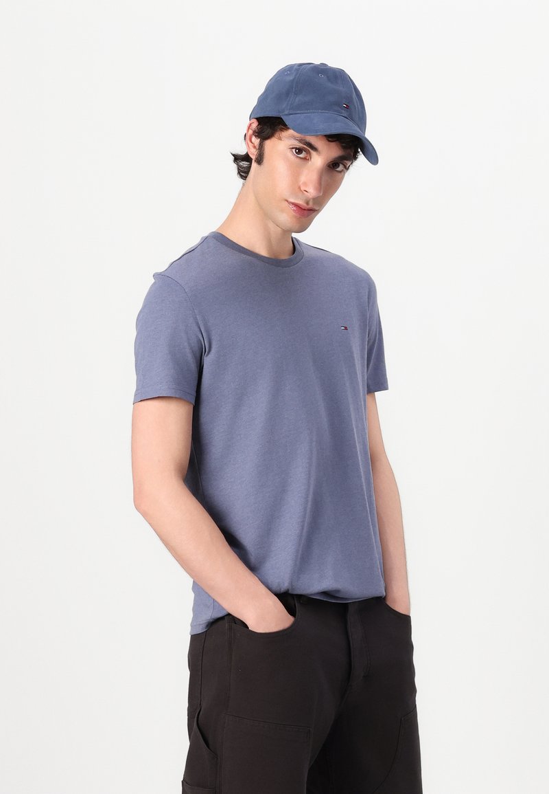 Pánské modré bavlněné tričko s krátkým rukávem a kulatým výstřihem, v kombinaci s modrou kšiltovkou s malým logem. Tmavé cargo kalhoty.