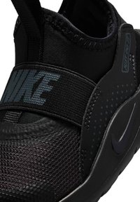 Sneaker noire Nike avec un tissu texturé, une bande élastique sur le pied et un swoosh Nike foncé sur la semelle et le panneau latéral.