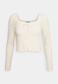 Pull court couleur crème avec un motif en losange texturé, manches longues, encolure carrée et un détail à nouer à l'avant. Ourlet festonné.