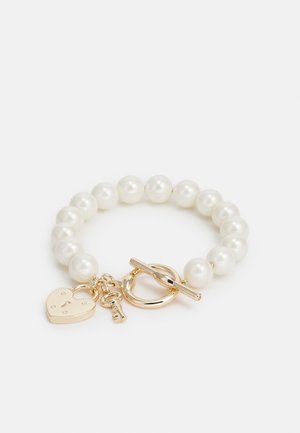 Bracciale di perle con chiusura a moschettone in oro. Presenta un ciondolo a forma di cuore con un dettaglio a chiave. Perle tonde e lisce di un bianco uniforme.
