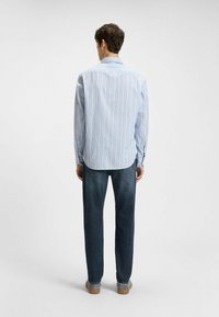 Lyseblå og hvid stribet skjorte med lange ærmer, krave og rundet kant, parret med mørkeblå jeans og beige sko.