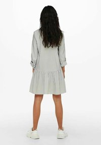 Koszulowa sukienka w paski z rozkloszowanym dołem, uszyta z lekkiego materiału. Ma długie rękawy podwinięte i luźny fason. Noszona z białymi trampkami.