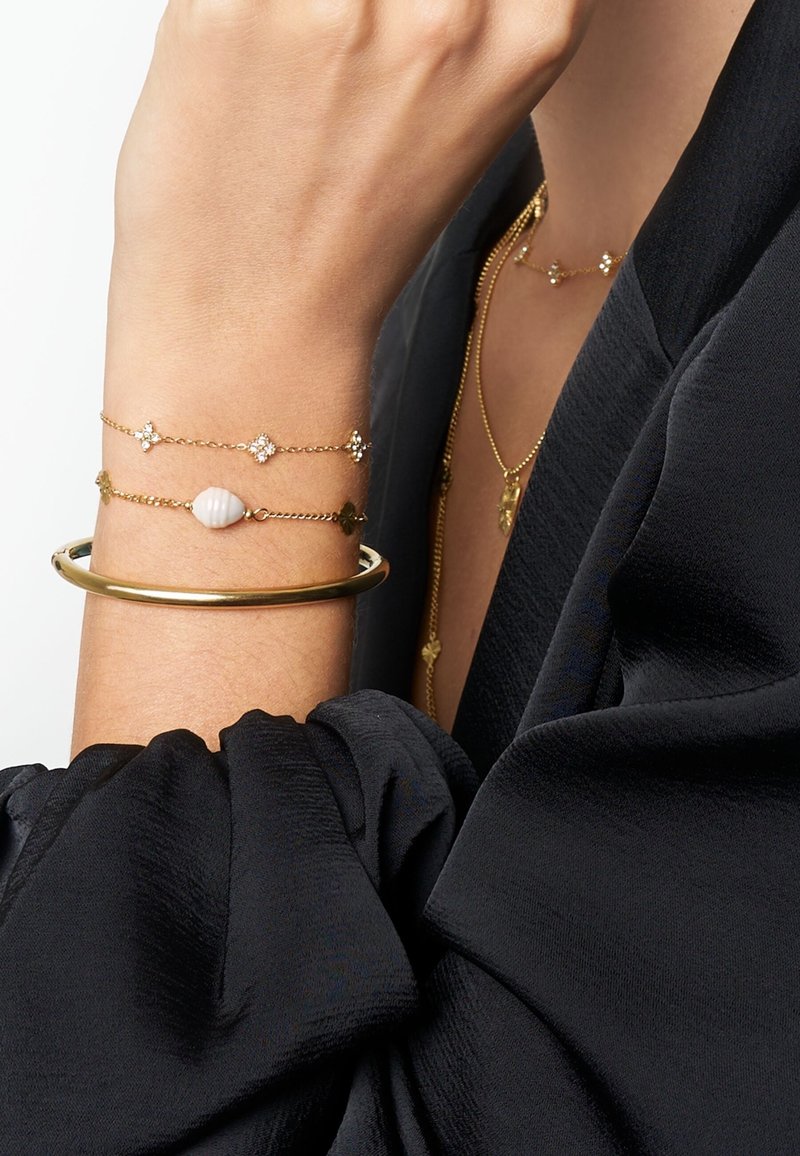 Gold-tone metal bangle with smooth finish; two delicate bracelets with tiny star accents, featuring a shell-like bead and sparkling elements.