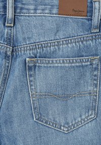 Jeans de mezclilla azul claro con un bolsillo trasero, costuras amarillas y una etiqueta de cuero marrón que dice "Pepe Jeans London". Tejido texturizado.