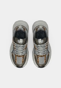 Αθλητικά παπούτσια με γκρι επάνω μέρος από δίχτυ, καφέ λεπτομέρειες με λεοπάρ σχέδιο, κορδόνια με μοτίβο και παχύ λευκό ενδιάμεσο πέλμα. Ορατή η σήμανση Buff.