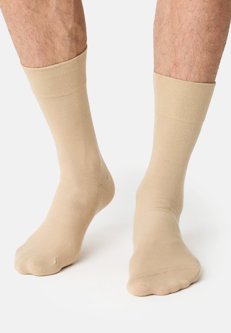 Calzini in cotone beige con polsini a coste, texture morbida e finitura liscia, progettati per adattarsi comodamente attorno al piede e alla caviglia.