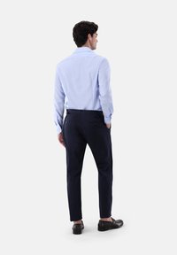 Camicia a maniche lunghe azzurro chiaro con polsini abbottonati, abbinata a pantaloni blu scuro. Tessuto liscio e vestibilità sartoriale con due tasche posteriori.