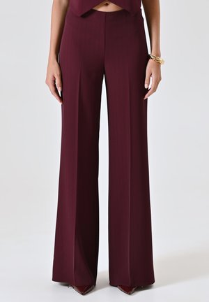 Pantaloni larghi bordeaux con una fantasia a righe sottili, in materiale liscio, vita alta e vestibilità sartoriale, abbinati a tacchi a punta.