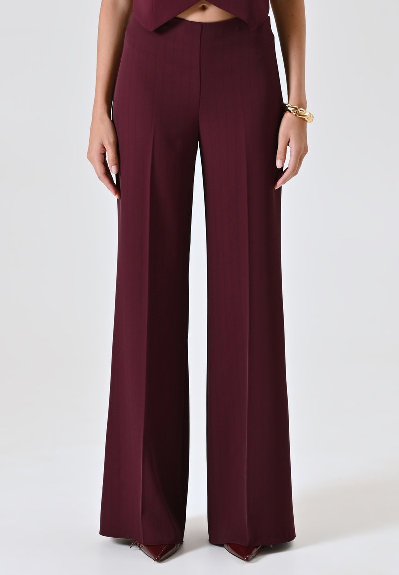 Pantaloni larghi bordeaux con una fantasia a righe sottili, in materiale liscio, vita alta e vestibilità sartoriale, abbinati a tacchi a punta.