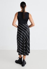 Musta hihaton yläosa yhdistettynä mustaan hameeseen, jossa on valkoiset vinoraitoja, viimeistelty mustilla nilkkureilla. Sileä kangaspinta.