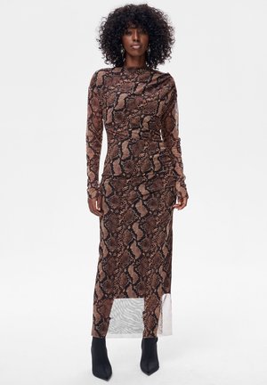 Brązowa midi sukienka w wężowy wzór z długimi rękawami, dopasowaną górą i przezroczystym dolnym panelem. Stylizowana z czarnymi botkami za kostkę.