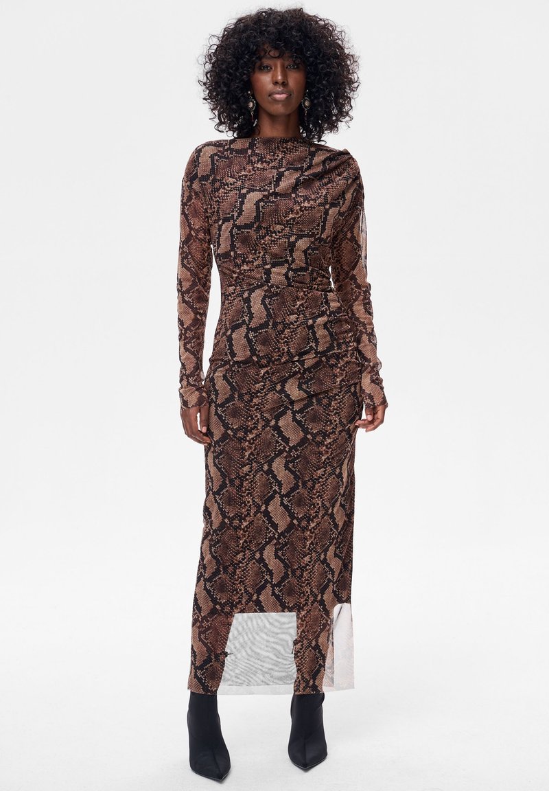 Brązowa midi sukienka w wężowy wzór z długimi rękawami, dopasowaną górą i przezroczystym dolnym panelem. Stylizowana z czarnymi botkami za kostkę.