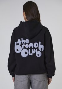 Felpa nera con cappuccio e una grande grafica bianca in caratteri a bolle che recita "the brunch club" sul retro. Presenta un cappuccio e una vestibilità comoda.