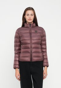 Pufjaka, kas ir nomāktā mauve krāsā, ar augstu apkakli, rāvējslēdzēja aizdari un horizontālu šuvju rakstu; tai ir mazs logo uz krūšu daļas.