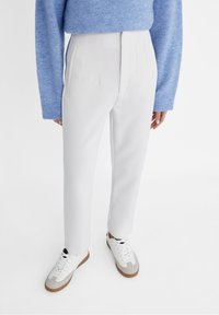 White trousers with a tailored fit, featuring front pleats. Paired with a blue wool sweater and gray-accented white sneakers.