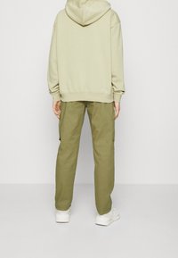 Sudadera oversized de color verde claro con capucha; pantalones cargo de color verde olivo de corte relajado con bolsillos laterales; zapatillas blancas completan el conjunto.