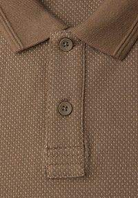 Hnědá polo košile s texturovanou tkaninou, se límcem, dvěma knoflíky a malým vzorovaným designem v světlejších odstínech.