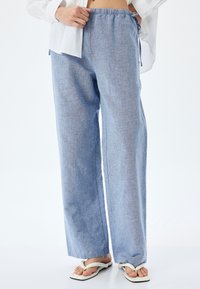 Lichtblauwe, wijde broek van geweven stof met een elastische tailleband en trekkoord. Kenmerkt zich door een gladde textuur en minimale stiknaden.