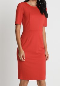 Czerwona dopasowana sukienka z krótkimi rękawami, okrągłym dekoltem i wyraźnymi przeszyciami. Wykonana z elastycznej tkaniny, ma długość do kolan i gładką fakturę.