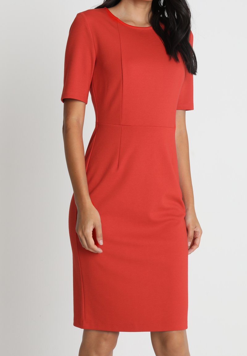 Czerwona dopasowana sukienka z krótkimi rękawami, okrągłym dekoltem i wyraźnymi przeszyciami. Wykonana z elastycznej tkaniny, ma długość do kolan i gładką fakturę.