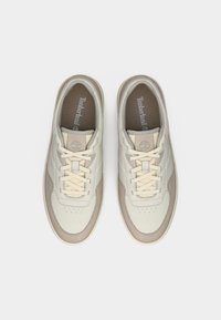 Μπεζ δερμάτινα αθλητικά παπούτσια με ανοιχτό καφέ λεπτομέρειες, στρογγυλεμένη μύτη, διάτρητο σχέδιο στην περιοχή της μύτης και κρέμ κορδόνια. Φέρουν το λογότυπο Timberland στο εσωτερικό.