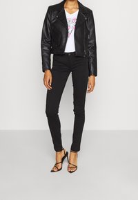 Chaqueta de cuero negra corta, camiseta gráfica blanca, jeans ajustados negros y sandalias de tacón alto negras con tiras. Diseño simple con detalles elegantes.