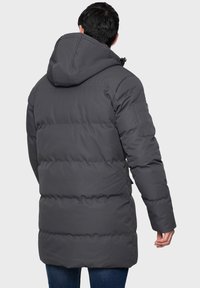 Graue Pufferjacke mit Kapuze, ausgestattet mit einem gesteppten Design, langen Ärmeln und einer Reißverschlusstasche am linken Arm.