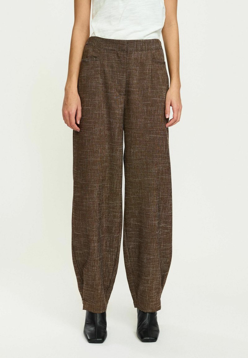 Brązowe spodnie o szerokich nogawkach z teksturowanym wzorem, charakteryzujące się luźnym krojem i elastycznym pasem. Połączone z czarnymi botkami za kostkę.