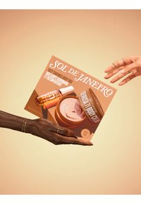 El paquete Cozy Cravings Body Duo en tonos cálidos muestra una botella de vidrio y un tarro, acentuados con oro. El empaque resalta la marca Sol de Janeiro.